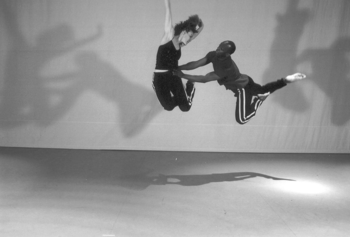 Two dancers leaping in unison, shadows thrown across the wall behind them