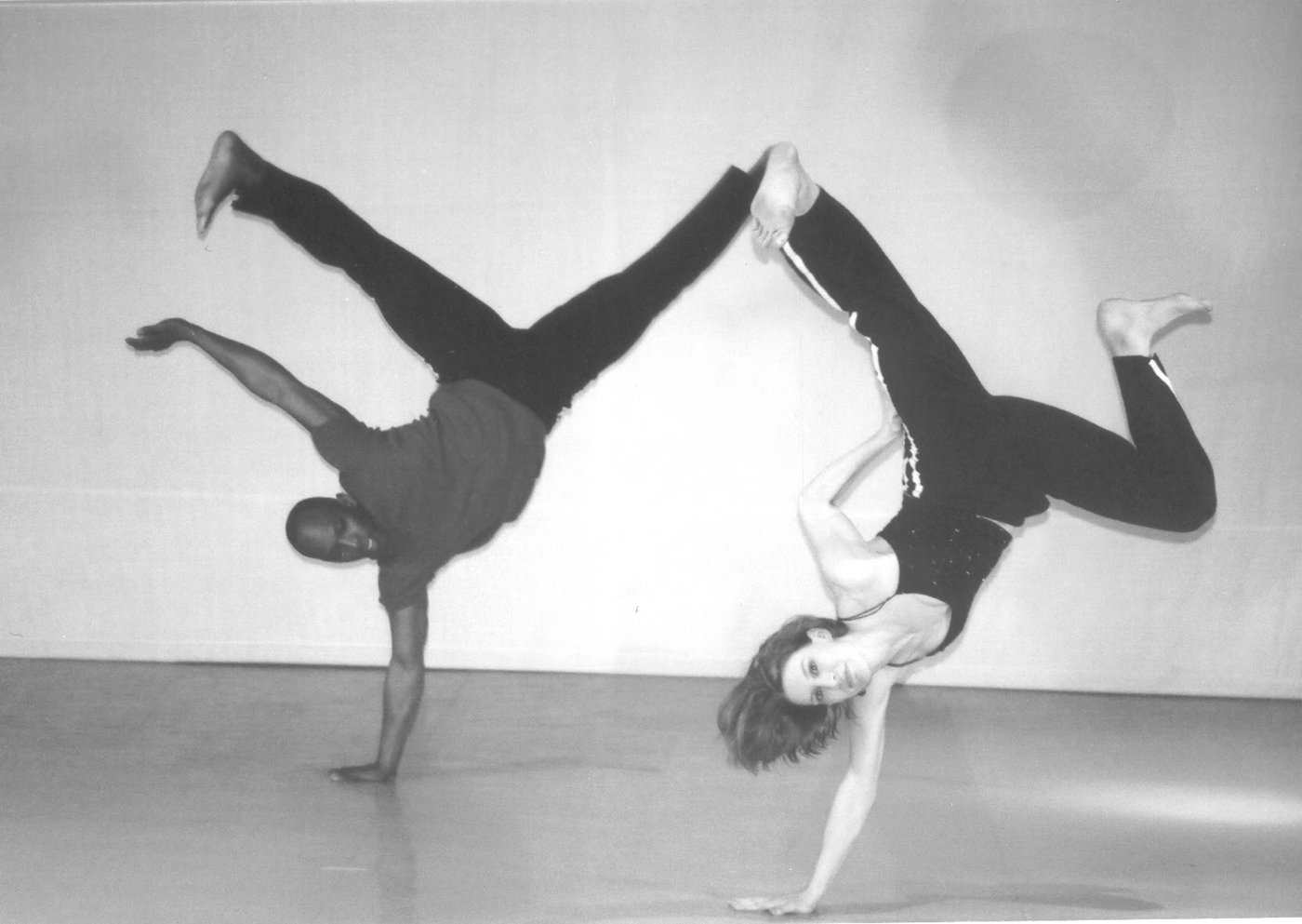 Boris Willis and a partner in mirrored handstands, legs splayed against a bright cyclorama