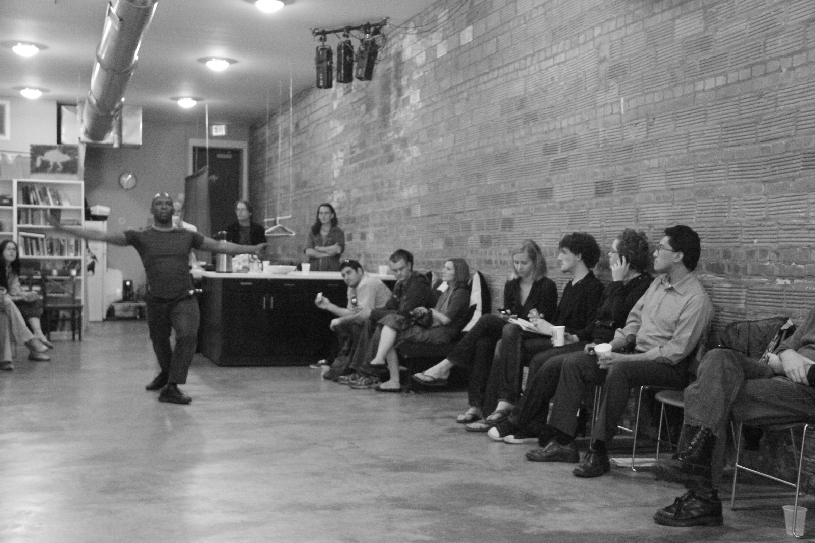 Boris Willis with one arm extended across the room toward the seated audience