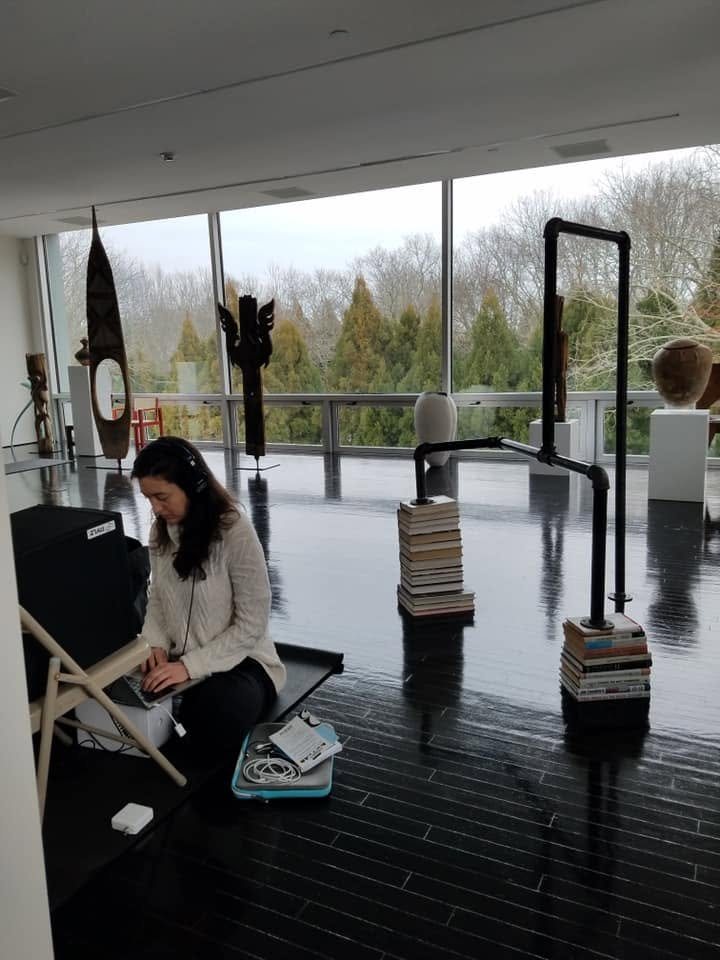 Erin Roy seated on the floor with a laptop, recording audio in the Watermill Center gallery
