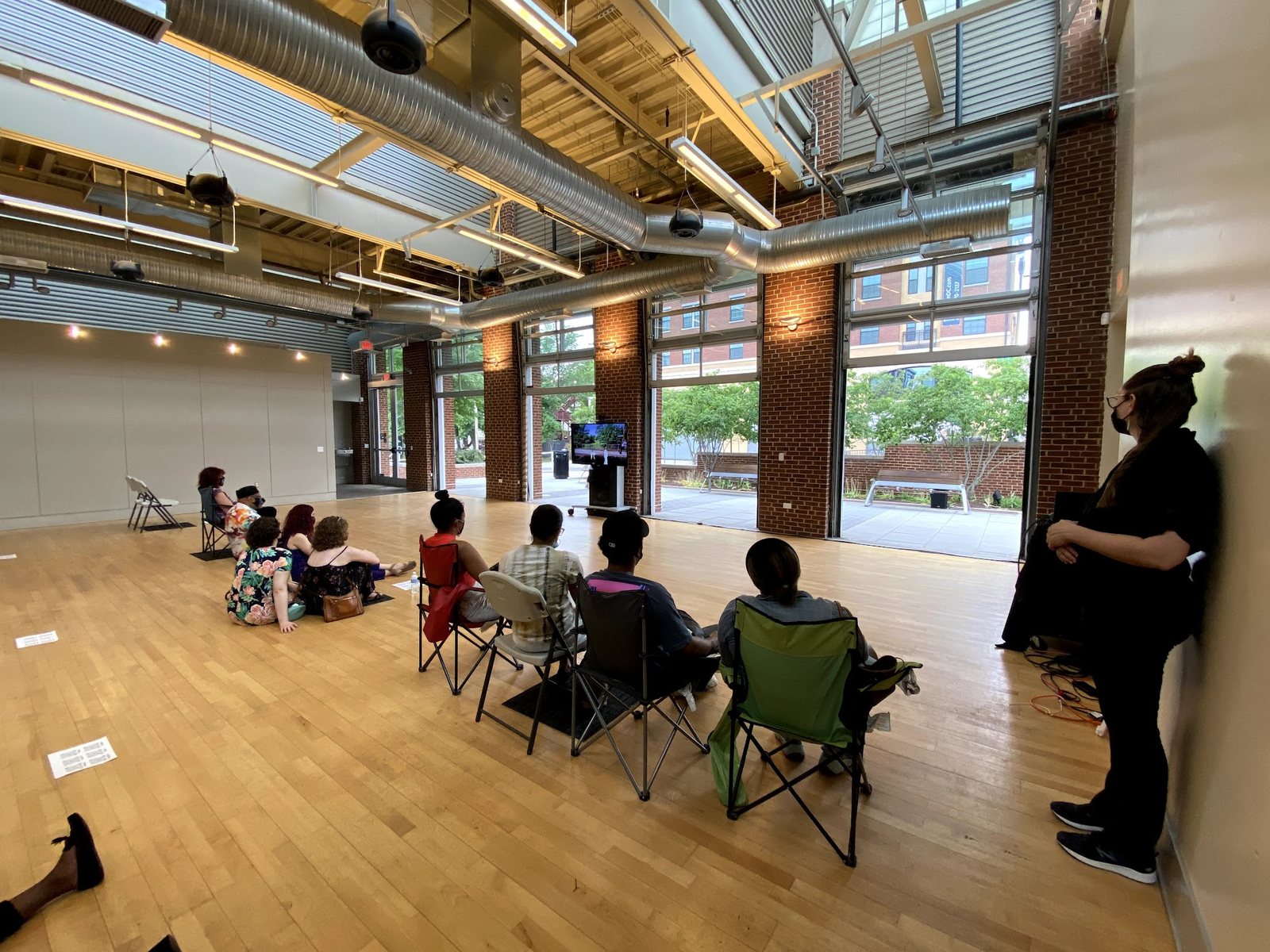 Audience members in folding chairs watching a screen in the open industrial hall at Dance Place