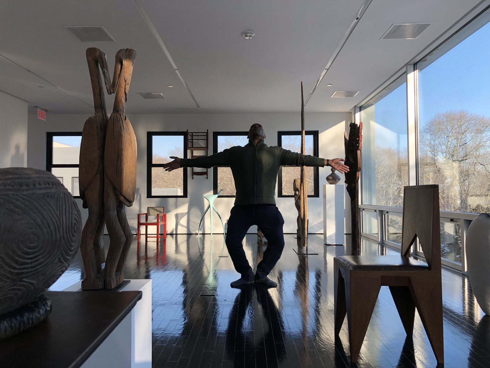 Dancer standing in a motion-capture calibration pose beside African sculptures and tall windows