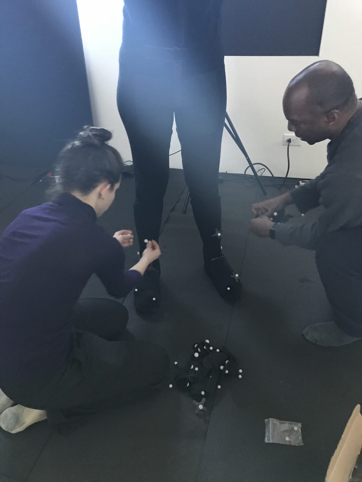 A collaborator adjusts motion-capture markers on a performer dressed in black